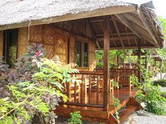 a small wooden house with a thatched roof and porch area in the middle of some plants