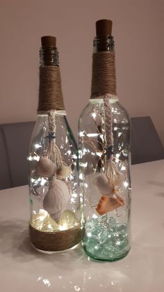 two bottles with seashells in them are sitting on a table together, one is filled with water and the other has lights