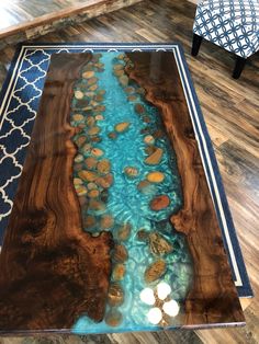 a coffee table with blue water and rocks in the middle on a wooden floor next to a chair