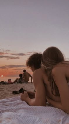 two people are sitting on the beach at sunset