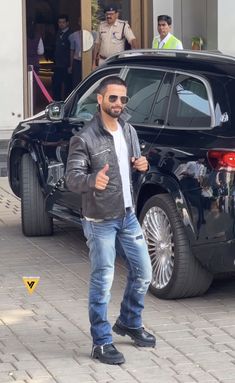 a man standing in front of a black suv giving the thumbs up sign with his hand