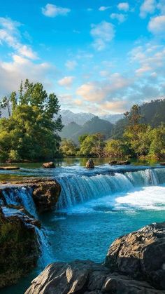 there is a waterfall in the middle of this river with blue water and green trees