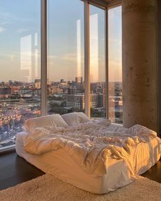 an unmade bed is in front of large windows overlooking the cityscape and skyscrapers