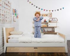 a child standing on top of a bed in a room with white walls and wooden floors