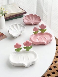 three ceramic flower vases sitting on top of a white table next to a book