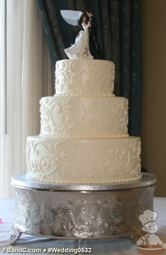 a white wedding cake sitting on top of a silver platter next to a window