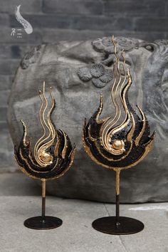 two gold and black vases sitting on top of each other next to a rock