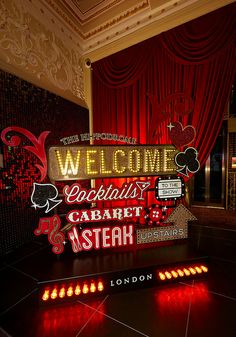 a welcome sign is lit up in front of a red drapeed curtain and floor