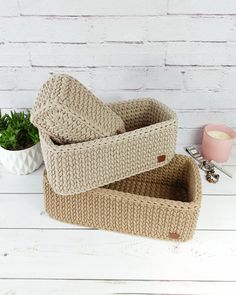 two knitted storage baskets sitting on top of a white table next to a potted plant