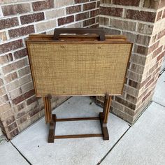 an old wooden and wicker suitcase sitting on a stand in front of a brick wall