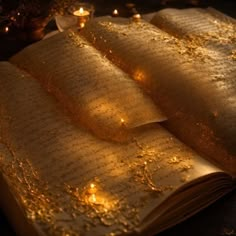 an open book with gold glitter on it and some candles around the pages in the background