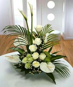 a vase with white flowers and greenery on a table