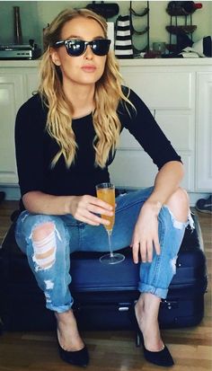 a woman sitting on top of a piece of luggage holding a drink in her hand