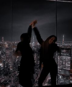 two people standing on top of a tall building in front of a cityscape