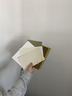 a person holding up some papers in front of a wall with white paint on it