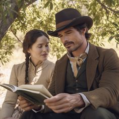 a man and woman sitting under a tree looking at something in their hands while reading a book