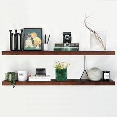 two wooden shelves with books, vases and other items on them against a white wall