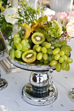 grapes, kiwis and other fruits are on a silver platter with flowers in the background