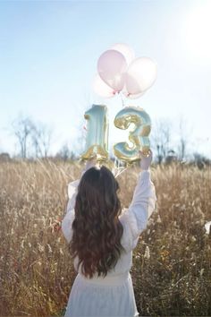 a girl in a white dress is holding balloons that spell the number thirteen and standing in a field