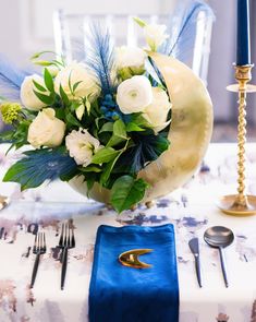 a table with blue napkins, silverware and white flowers in a vase on it