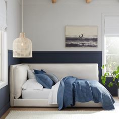 a white bed with blue sheets and pillows in a room next to a painting on the wall