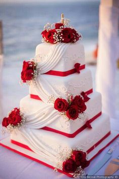 a three tiered wedding cake with red roses on top