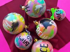 four ornaments with words painted on them are sitting on a red cloth next to a pink background