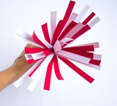 a hand is holding a red and white paper pinwheel that looks like it has been folded