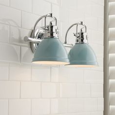 two light fixtures mounted on the wall in a white tiled bathroom with blue shades and metal fittings