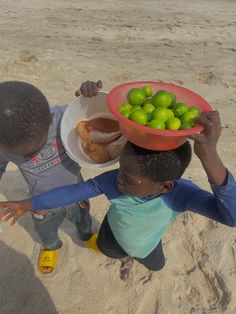 two young boys on the beach holding up bowls with limes in them and bread