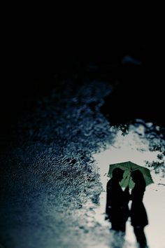 two people are standing under an umbrella in the rain, with their shadows on the ground