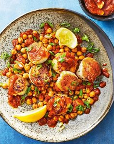 a white plate topped with lots of food next to a bowl filled with sauce and lemon wedges