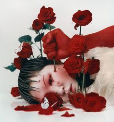 a young boy laying on the ground surrounded by red roses with his hands over him