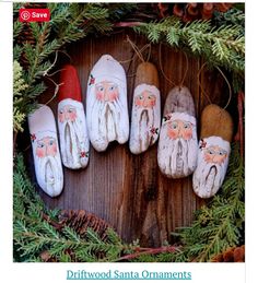 painted rocks in the shape of santa claus surrounded by evergreen branches and pine cones on a wooden surface