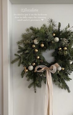 a christmas wreath hanging on the wall next to a white door with a ribbon tied around it