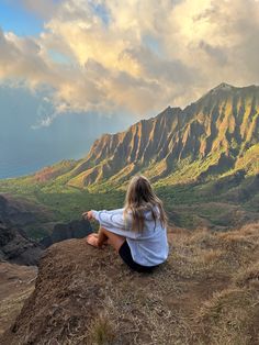 a woman sitting on top of a hill looking at the mountains