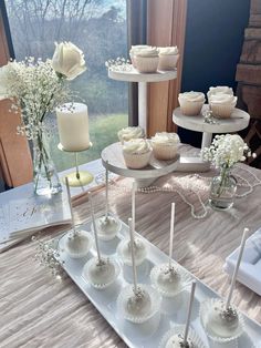 cupcakes and candles on a table in front of a window, with flowers