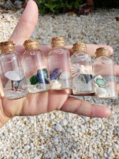 small bottles filled with sand and sea shells in the palm of someone's hand