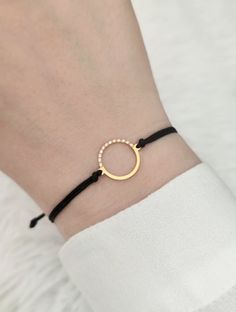 a woman wearing a black cord bracelet with a gold circle on it