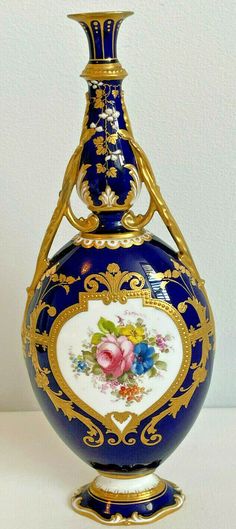 a blue and gold vase sitting on top of a white table next to a wall