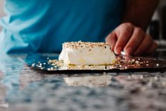 a person is decorating a cake with white frosting and sprinkles