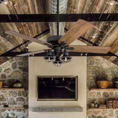 a ceiling fan is hanging in front of a fireplace with stone walls and exposed wood beams