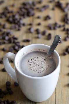 a cup of coffee with a spoon in it sitting on a wooden table surrounded by chocolate chips