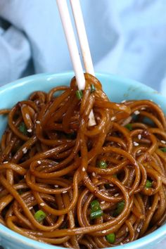 a bowl filled with noodles and chopsticks on top of a blue table cloth