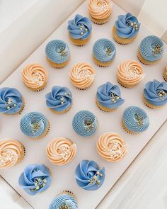 a box filled with blue and yellow cupcakes on top of a white table