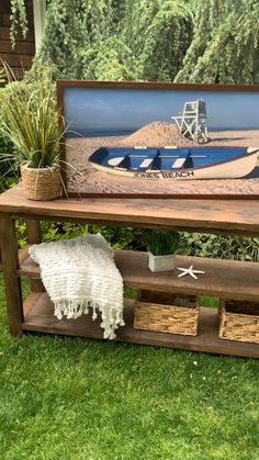 a wooden bench with a painting on it in the grass near some plants and other items