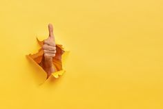 a person's thumb up through a hole in yellow paper