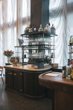 an old fashioned bar with lots of bottles and glasses on the top shelf, in front of a window