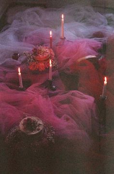 candles are lit on a table covered in pink tulle