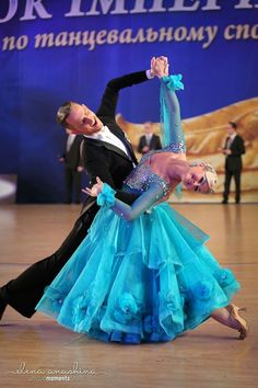 two people in ballroom clothes doing a dance on the floor with their arms around each other